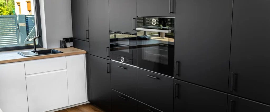 Minimalist kitchen with matte black floor-to-ceiling cabinets, built-in oven and microwave, and black hardware.