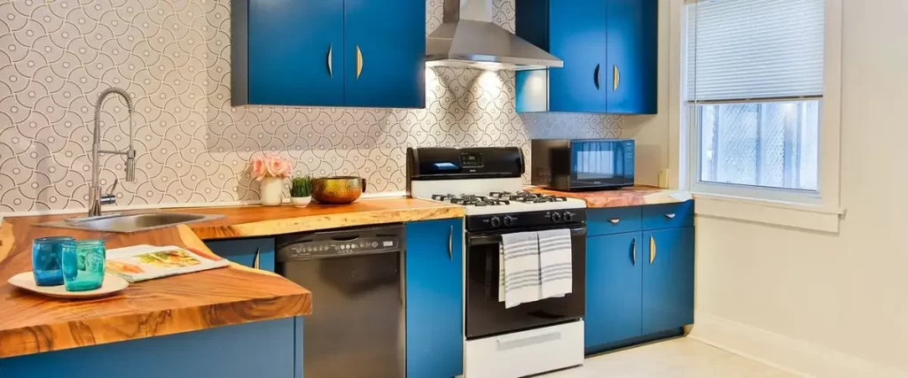 Modern kitchen with vibrant blue cabinets, wooden countertops, and stainless steel appliances including a gas stove, range hood, microwave, and dishwasher.