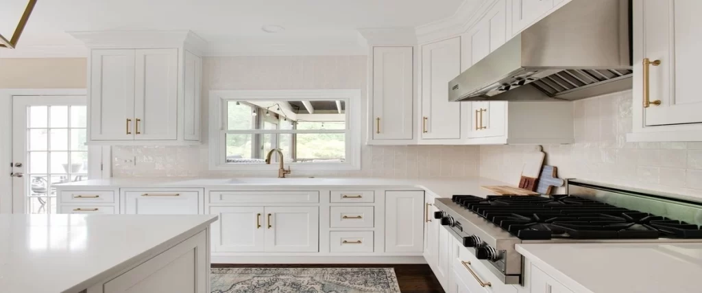 Bright, modern kitchen with white cabinets, gold hardware, and a large stainless steel gas range beneath a matching hood.
