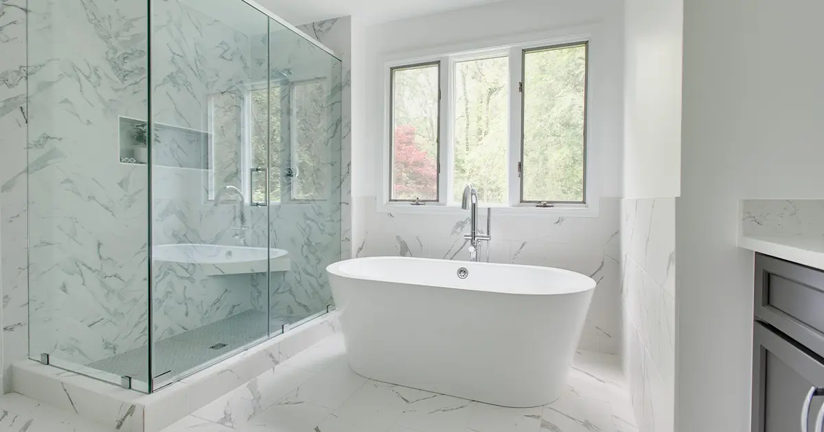 Modern luxurious bathroom with marble walk-in shower and white freestanding tub against a large white wall with windows