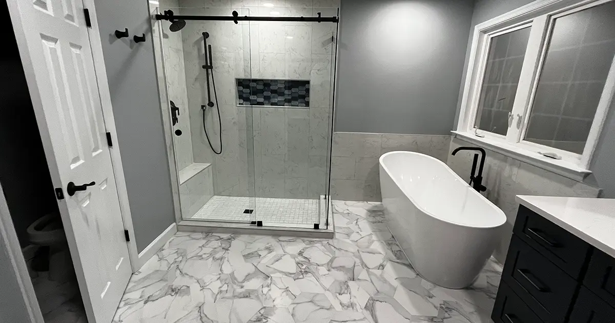 White and gray bathroom remodel with marble and freestanding white tub against large window
