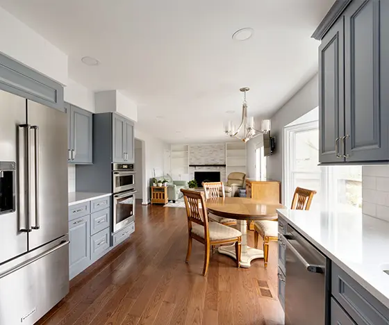 large kitchen and open space area with new custom cabinets in gray color, custom flooring, and fireplace in the background