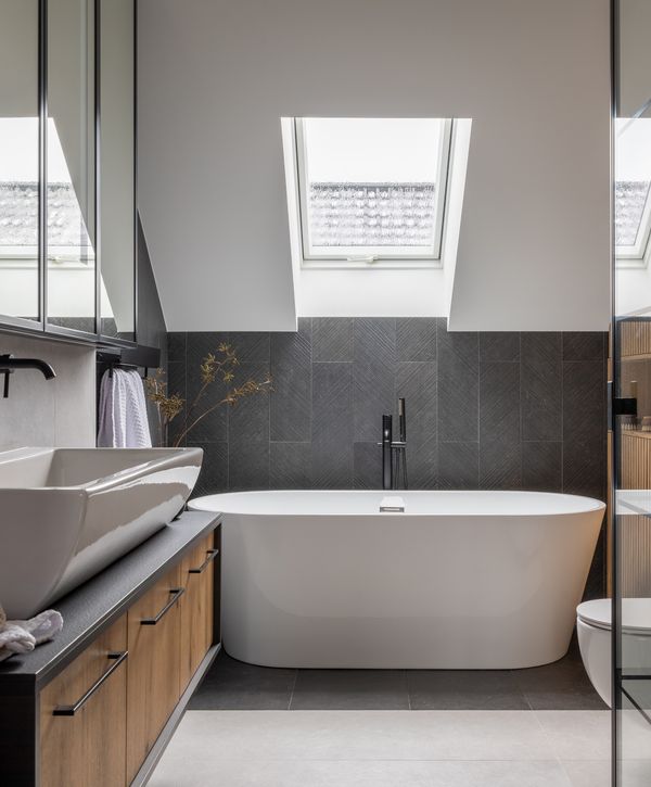 Modern bathroom featuring a freestanding tub under a skylight, with sleek black and wood accents.