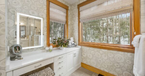 Bright modern bathroom, forest view, dual vanity, patterned wallpaper.
