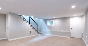 Modern basement interior, beige carpet, white walls, staircase, blue railing.