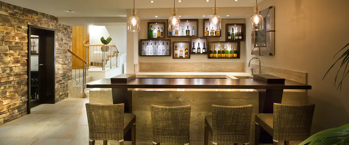 Modern home bar, pendant lights, stone wall, wicker stools.