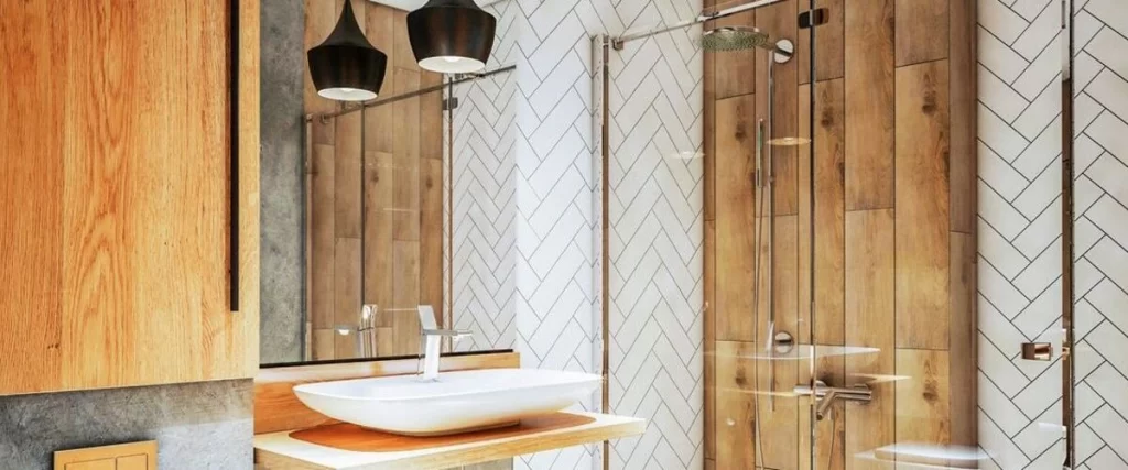 A modern bathroom featuring a white herringbone tile pattern on the walls, contrasted with warm wood plank tiles inside the glass shower enclosure.