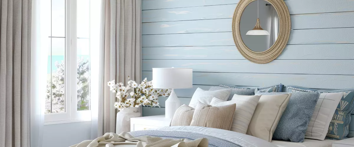 Beautiful interior of a light blue and white bedroom with shiplap wall, a mirror above the nightstand and a window with curtains, home decor