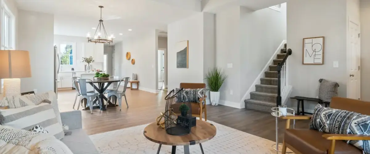 An open-concept living space featuring a bright living room with a light grey sofa, leather armchairs, a round wooden coffee table, and a neutral rug.