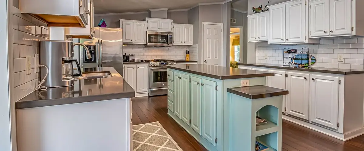 A contemporary kitchen renovation showcasing a light blue center island with dark countertops, white subway tile backsplash, and matching white cabinetry.