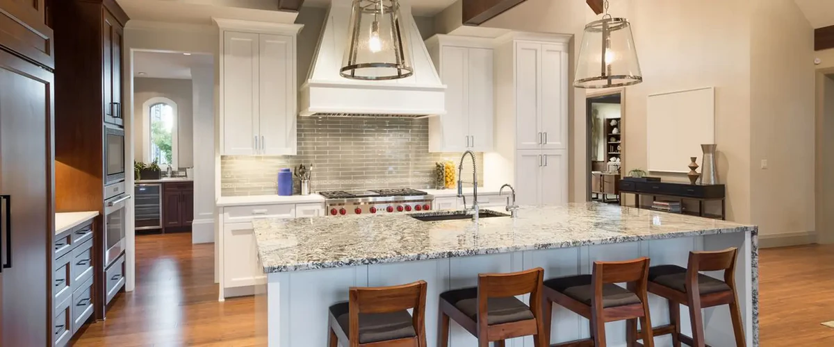 A luxury kitchen layout showcasing a massive granite island with seating for four, white cabinetry, a stylish backsplash, and designer glass pendant lights.