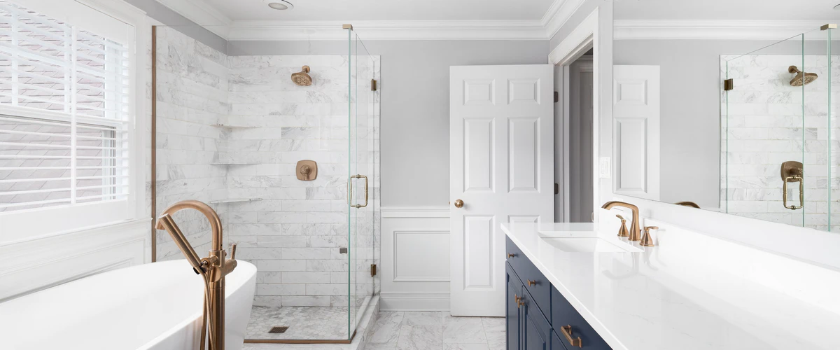 Spacious modern bathroom featuring a white marble walk-in shower with gold hardware, a navy blue vanity, and a freestanding soaking tub.