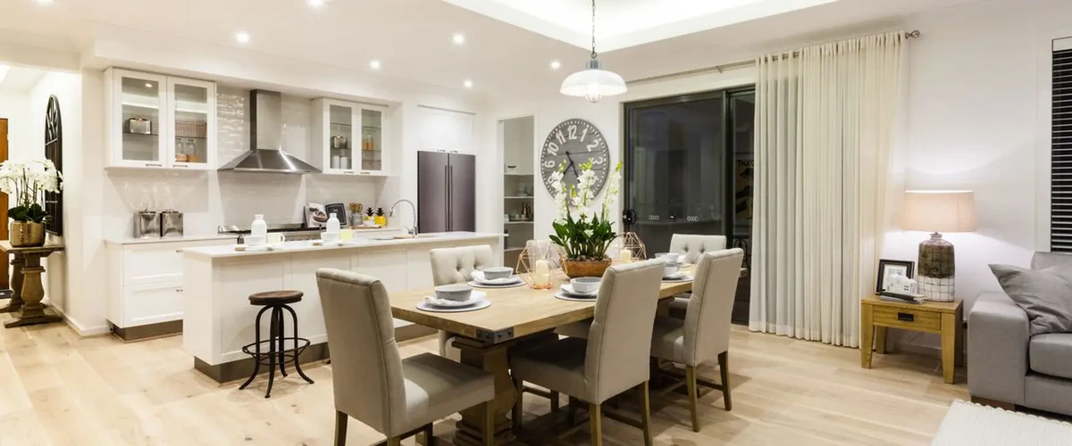 A bright modern open-concept kitchen and dining area with white minimalist cabinetry, a large light-wood dining table with upholstered chairs, and a sliding glass door.