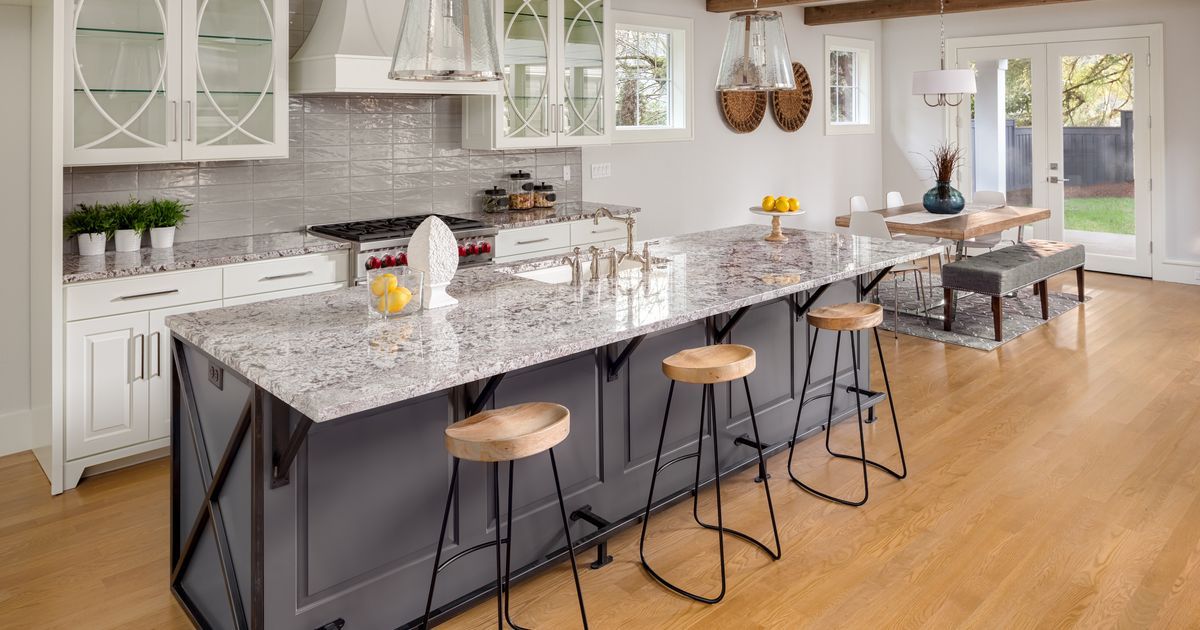 A spacious modern kitchen featuring a large grey island with granite countertops and wooden barstools, showcasing a high-end kitchen remodel cost investment.
