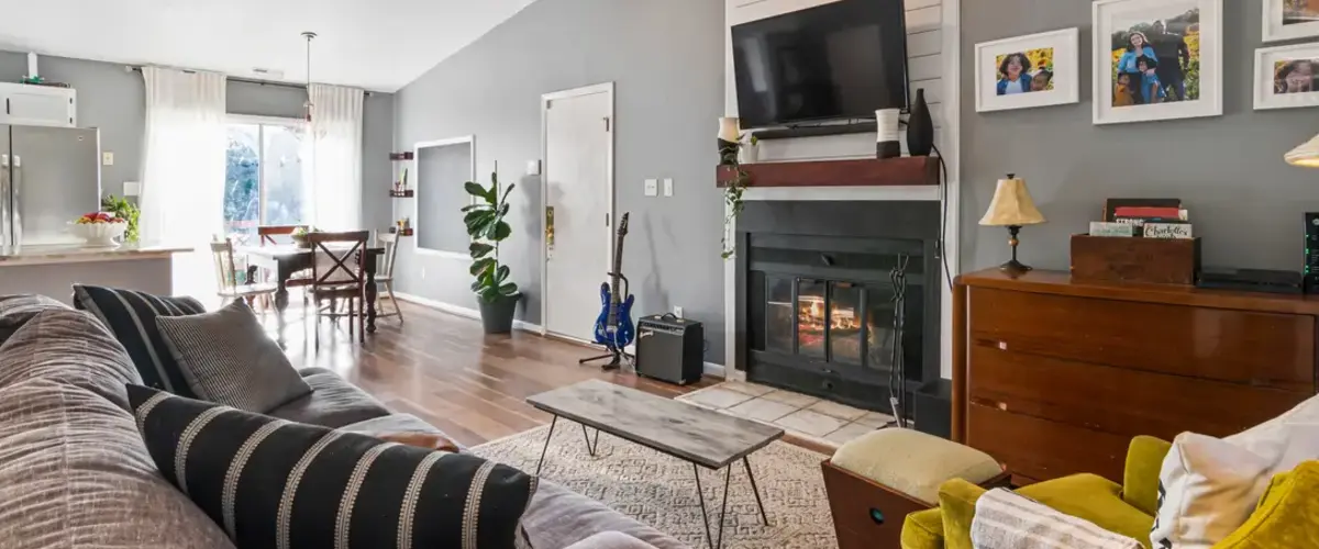 A spacious open-concept home interior showing a living area with a gray wall, a black fireplace topped with a television, and a dining table set near a bright sliding glass door.