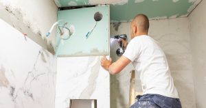A professional contractor using a power drill to install large white marble wall tiles during a home renovation project to estimate bathroom remodel cost.
