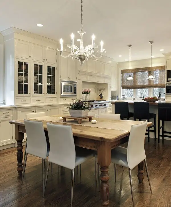 A spacious open concept kitchen remodeling in Burke, VA featuring a rustic wood dining table, white custom cabinetry, and an elegant glass chandelier.