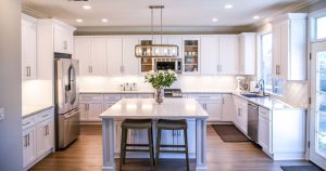 A bright, open-concept kitchen featuring white shaker cabinets, a large central island with stools, and a stylish rectangular glass chandelier highlighting the kitchen remodel cost for modern upgrades.