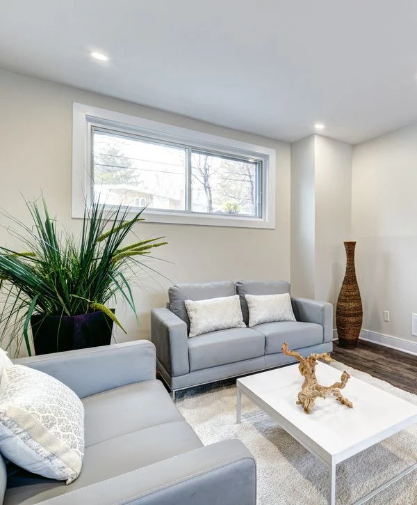 A bright, modern basement remodeling in Burke, VA featuring a grey sofa, white coffee table, and large window with natural light.