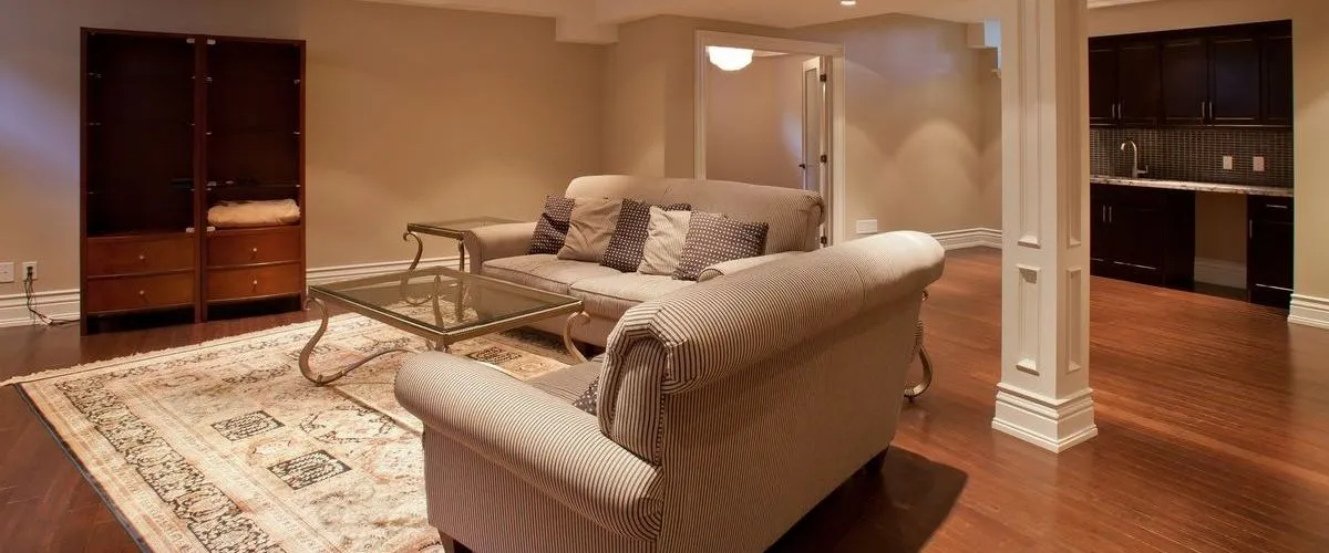 Spacious finished basement featuring a large open floor plan with hardwood floors, comfortable seating, and a background kitchenette.