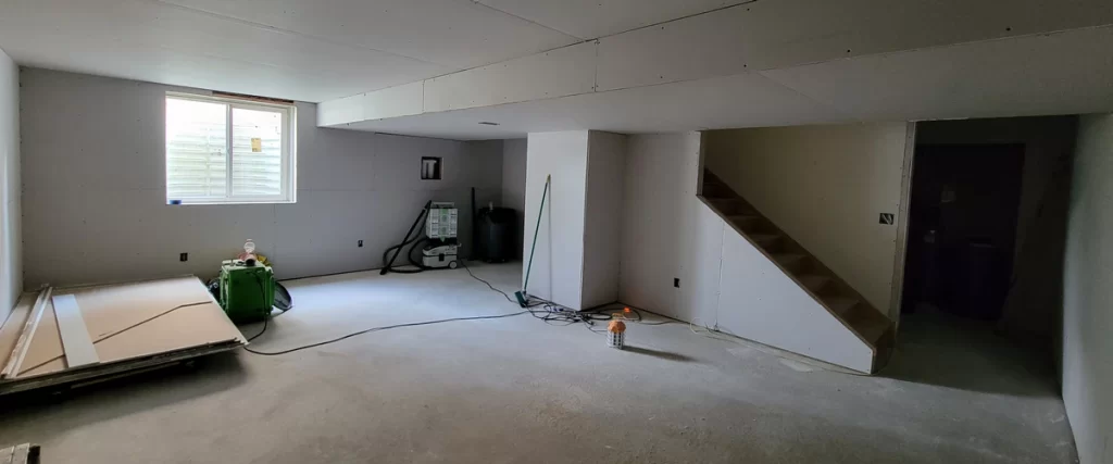 A clean and contemporary basement remodeling project showing a comfortable gray sectional sofa and bright egress window.