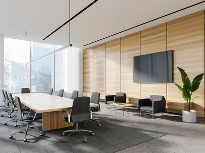 A modern corporate boardroom displaying a mid-range commercial renovation, complete with a long light-wood conference table, black chairs, a wood-paneled accent wall with a monitor, and a casual seating area.