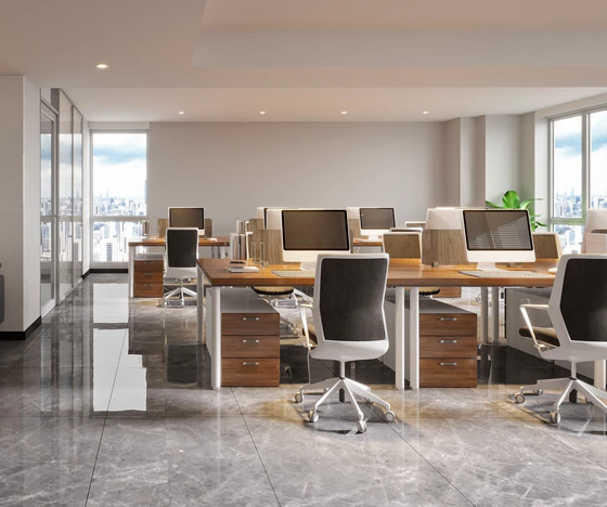 A bright, newly updated modern open-plan office space featuring wooden desks, white ergonomic chairs, polished stone floors, and large windows overlooking a city skyline, showcasing the results of a recent commercial remodeling.